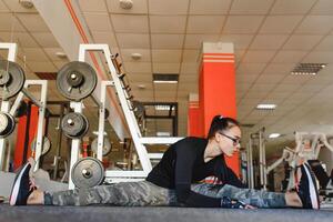 bonito niña haciendo extensión ejercicios en el piso a el gimnasia. foto