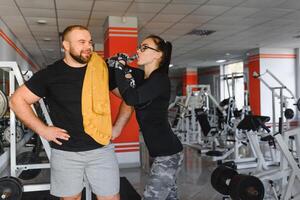 Fitness, sports, exercises and weightlifting. Concept - a young woman and a young man with dumbbells sweeping muscles in the gym photo