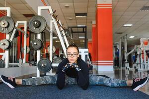 bonito niña haciendo extensión ejercicios en el piso a el gimnasia. foto