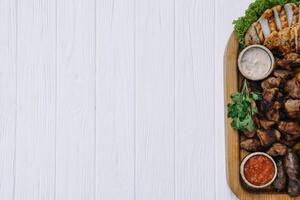 Most meat dish - beef kebabs, sausages, grilled mushrooms, potatoes, tomatoes and sauce. The best choice for a beer. Close-up on a white wooden background photo