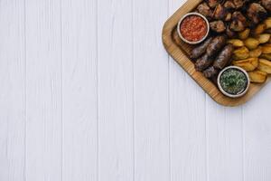 Most meat dish - beef kebabs, sausages, grilled mushrooms, potatoes, tomatoes and sauce. The best choice for a beer. Close-up on a white wooden background photo