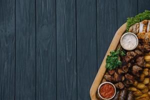 Most meat dish - beef kebabs, sausages, grilled mushrooms, potatoes, tomatoes and sauce. The best choice for a beer. Close-up on a wooden background. photo