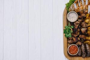 Most meat dish - beef kebabs, sausages, grilled mushrooms, potatoes, tomatoes and sauce. The best choice for a beer. Close-up on a white wooden background. photo