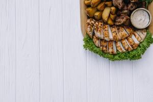 Most meat dish - beef kebabs, sausages, grilled mushrooms, potatoes, tomatoes and sauce. The best choice for a beer. Close-up on a white wooden background. photo