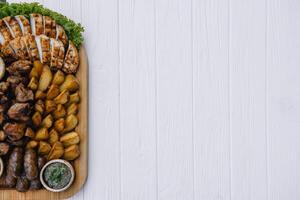 Most meat dish - beef kebabs, sausages, grilled mushrooms, potatoes, tomatoes and sauce. The best choice for a beer. Close-up on a white wooden background. photo