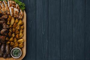 Most meat dish - beef kebabs, sausages, grilled mushrooms, potatoes, tomatoes and sauce. The best choice for a beer. Close-up on a wooden background. photo