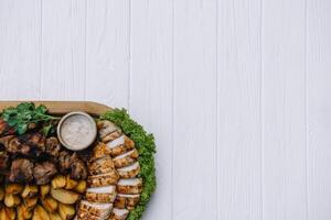 Most meat dish - beef kebabs, sausages, grilled mushrooms, potatoes, tomatoes and sauce. The best choice for a beer. Close-up on a white wooden background. photo