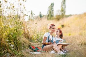 Young attractive mother teaches daughter painting in summer park. Outdoors activity for school age children concept. photo