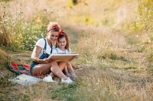 Beauty mother paint with her little daughter. Stylish woman drawing the picture with little girl. Cute kid in a white t-shirt and blue jeans. Mother's Day. photo