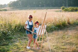 madre enseña hija pintar en parque. soleado naturaleza, mamá y hija pintar un imagen en un parque , pintura un pequeño niño, niño creatividad. de la madre día. foto