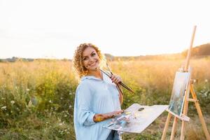 Pretty woman is painting. Open air session. Cute woman draws a picture at sunset. girl artist. photo