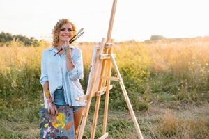 Pretty woman is painting. Open air session. Cute woman draws a picture at sunset. girl artist photo