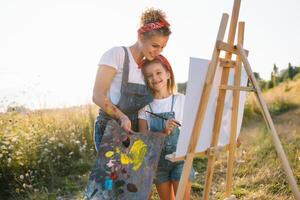 Beauty mother paint with her little daughter. Stylish woman drawing the picture with little girl. Cute kid in a white t-shirt and blue jeans. Mother's Day. photo