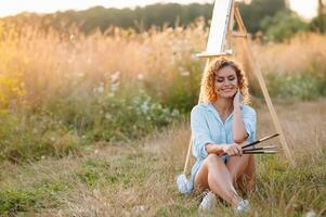 Pretty woman is painting. Open air session. Cute woman draws a picture at sunset. girl artist. photo