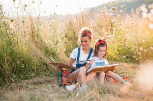 Young attractive mother teaches daughter painting in summer park. Outdoors activity for school age children concept. photo