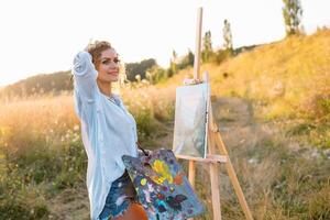Pretty woman is painting. Open air session. Cute woman draws a picture at sunset. girl artist photo