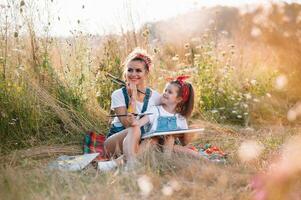 Young attractive mother teaches daughter painting in summer park. Outdoors activity for school age children concept. photo