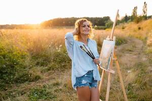 Pretty talented female painter painting on easel, making colorful sketches, creating marine landscape. Beautiful female artist painting with watercolor paints. Creativity and imagination concept photo