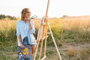 Pretty talented female painter painting on easel, making colorful sketches, creating marine landscape. Beautiful female artist painting with watercolor paints. Creativity and imagination concept photo