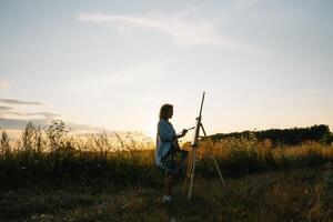 Pretty woman is painting. Open air session. Cute woman draws a picture at sunset. girl artist. photo