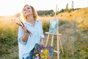 Pretty woman is painting. Open air session. Cute woman draws a picture at sunset. girl artist. photo