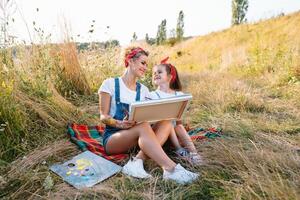 belleza madre pintar con su pequeño hija. elegante mujer dibujo el imagen con pequeño muchacha. linda niño en un blanco camiseta y azul vaqueros. de la madre día. foto