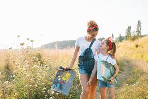 Beauty mother paint with her little daughter. Stylish woman drawing the picture with little girl. Cute kid in a white t-shirt and blue jeans. Mother's Day. photo