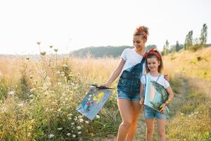 belleza madre pintar con su pequeño hija. elegante mujer dibujo el imagen con pequeño muchacha. linda niño en un blanco camiseta y azul vaqueros. de la madre día. foto