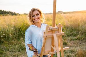 Pretty woman is painting. Open air session. Cute woman draws a picture at sunset. girl artist. photo