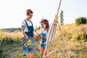 Sunny nature, mom and daughter paint a picture in a park , painting a Little Child, Child Creativity. Mother's Day. photo