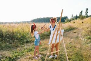 Beauty mother paint with her little daughter. Stylish woman drawing the picture with little girl. Cute kid in a white t-shirt and blue jeans. Mother's Day. photo