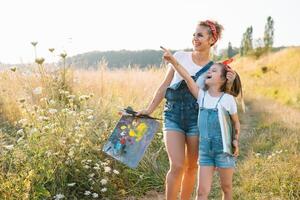 mother teaches daughter paint in park. photo