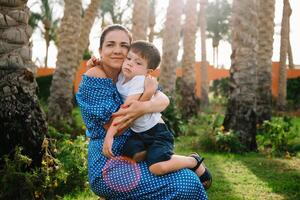 Stylish mother and handsome son having fun on a green lawn. Happy family concept. Beauty nature scene with family outdoor lifestyle. Happy family resting together. Mothers day photo