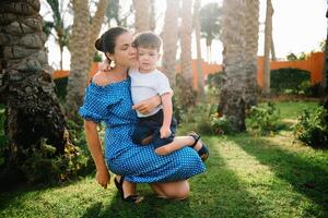 Stylish mother and handsome son having fun on a green lawn. Happy family concept. Beauty nature scene with family outdoor lifestyle. Happy family resting together. Mothers day photo