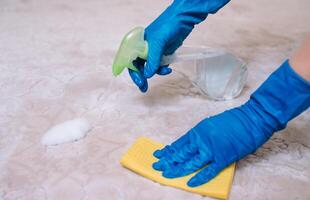 people, housework and housekeeping concept - close up of woman in rubber gloves with cloth and derergent spray cleaning carpet at home. close up of woman with cloth cleaning carpet photo