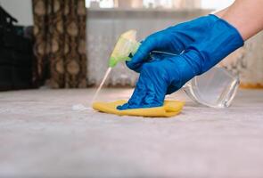 people, housework and housekeeping concept - close up of woman in rubber gloves with cloth and derergent spray cleaning carpet at home. close up of woman with cloth cleaning carpet photo