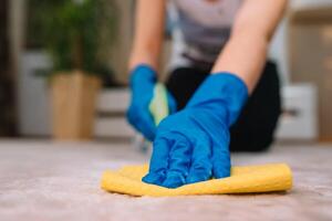 people, housework and housekeeping concept - close up of woman in rubber gloves with cloth and derergent spray cleaning carpet at home. close up of woman with cloth cleaning carpet photo