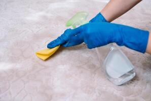 people, housework and housekeeping concept - close up of woman in rubber gloves with cloth and derergent spray cleaning carpet at home. close up of woman with cloth cleaning carpet photo