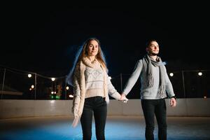 Man and woman young family Happy smiles hold hands skate on winter rink at night, with bokeh lights. photo