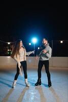 Man and woman young family Happy smiles hold hands skate on winter rink at night, with bokeh lights. photo