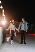 Winter skates, loving couple holding hands and rolling on rink. Illumination in background, night. Concept training. photo