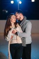 Theme ice skating rink and loving couple. meeting young, stylish people ride by hand in crowd on city skating rink lit by light bulbs and lights. Ice skating in winter for Christmas on ice arena. photo