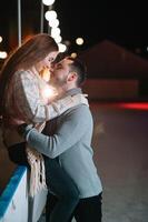 Theme ice skating rink and loving couple. meeting young, stylish people ride by hand in crowd on city skating rink lit by light bulbs and lights. Ice skating in winter for Christmas on ice arena. photo