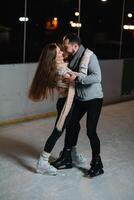 Man and woman young family Happy smiles hold hands skate on winter rink at night, with bokeh lights. photo