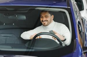 Handsome bearded businessman is sitting in a new car in car dealership photo