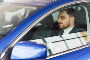 Handsome bearded businessman is sitting in a new car in car dealership photo