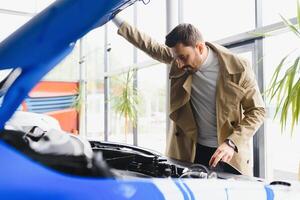 Mid adult car salesman showing the engine to client at the dealership photo