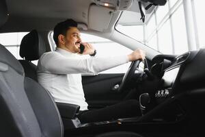 Nice business talk. Handsome young businessman talking on his smart phone and smiling while sitting on the front seat photo