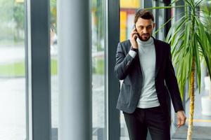 Young businessman standing in office hall and talking on phone photo