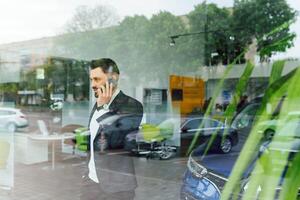 el coche muestra el personaje de un hombre. confidente éxito elegante negocio hombre en lleno traje y con teléfono en mano en pie cerca nuevo azul coche mira lejos foto